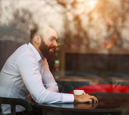 Young joyful dreamy male businessman in cafe, view through a window with reflections on the glassの写真素材