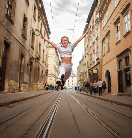 Athletic girl gymnast jumping in the street of the old city in summerの写真素材