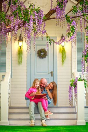 Parents mother and father read a book with their daughter in the courtyard of a traditional spring home, parenting education of children, family leisure lifestyleの写真素材
