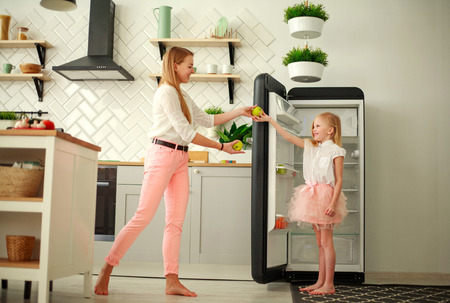 Mother and daughter in the kitchen put fruits and apples in the refrigerator, home family healthy lifestyleの写真素材