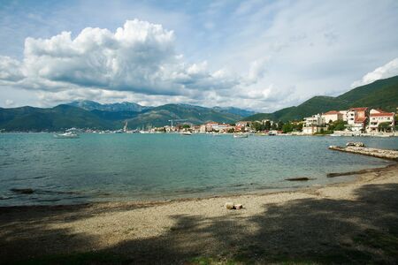 Bay in a seaside town with boats, houses in green mountains on blue sky,Tivat, Montenegro