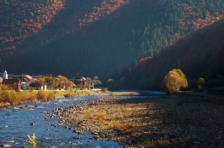 River in a mountain valley covered with autumnal colorful forest at sunrise