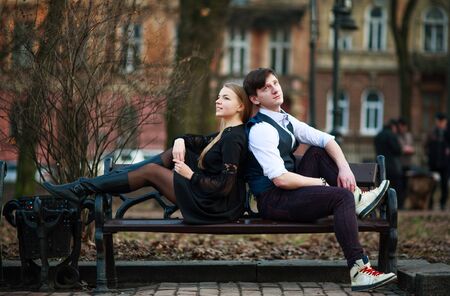 Loving young couple, guy and girl are sitting on a bench in a city parkの写真素材