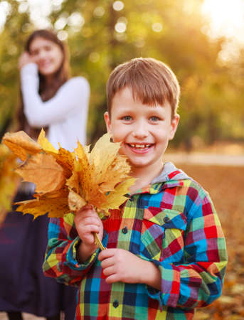 Portrait of a happy boy child with fallen yellow autumn foliage in an autumn city forest parkの写真素材