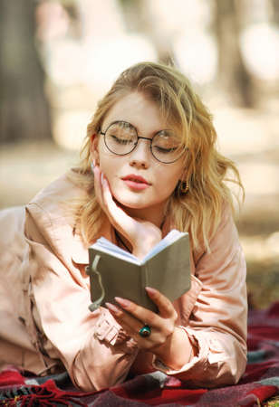 Intelligent girl student thoughtfully reads a book, diary in a city park