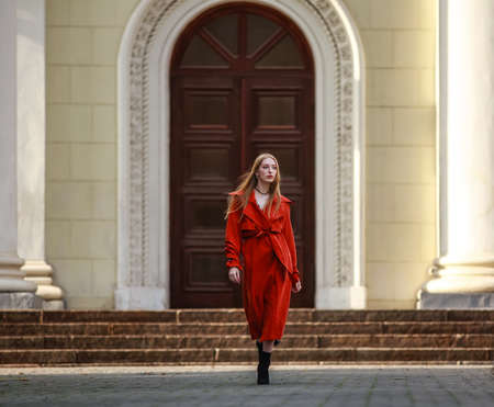 Elegant girl model in a fashionable coat terracotta color goes on city streetの写真素材