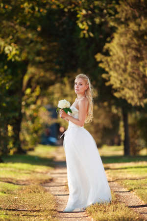 Young woman bride in a white wedding dress in a forest park with a bouquet of flowersの写真素材