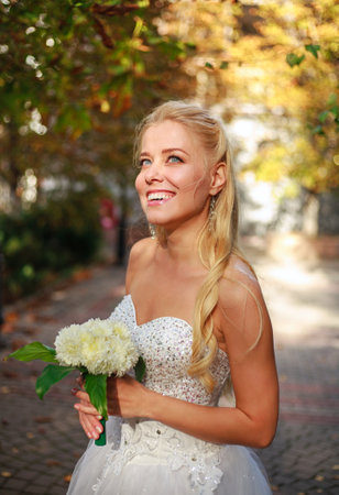 Dreamy bride in a white dress and with a bouquet of flowers in anticipation of a joyful eventの写真素材