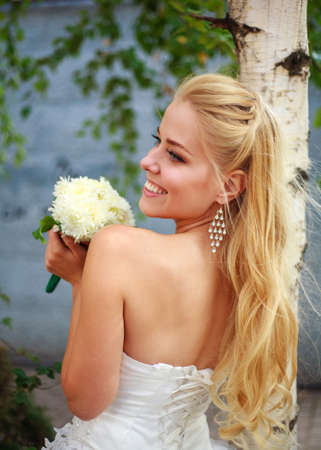 Dreamy bride in a white dress and with a bouquet of flowers in anticipation of a joyful eventの写真素材