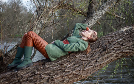 Beautiful lady in rustic style clothes on a tree by the riverの写真素材