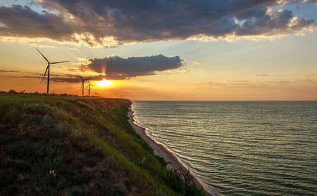 Cliffs over the seashore extending to the horizon with electricity windmills on the background of a...