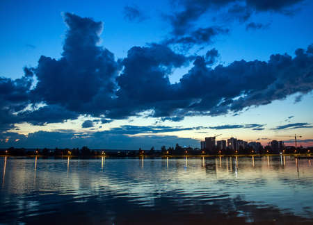 Urban landscape, cityscape buildings under construction on the background of the lake and sunset dramatic skyの写真素材