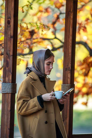 Luxurious young woman in retro fashion style, in a beige coat and scarf on her head, in a cafe on a...