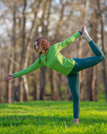 Young woman yogi in park on the green grass doing fitness exercises stretching the body, healthy lifestyle in pure natureの写真素材
