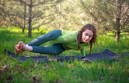 Young woman doing yoga fitness exercises outdoors, on green fresh grass on the background of...