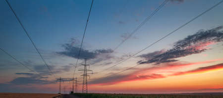 Electrical power pylons and wire lines on the road at dramatic sunset sky background