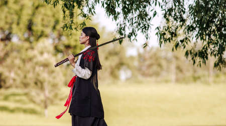 Young asian woman in traditional kimono trains in a fighting stance close-up portrait with katana sword samurai warrior girl in green summer gardenの写真素材