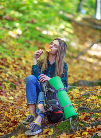 Pensive girl in casual style with a backpack walks, travels and hikes in a beautiful sunny forest park aloneの写真素材