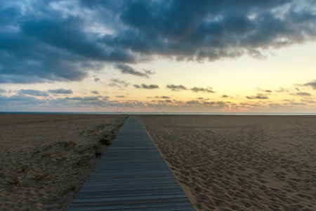 Wooden platform, in the middle of a sandy beach, leading to the sea, against a colorful twilight skyの写真素材