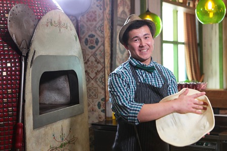 A young guy, a restaurant worker or cafe makes pizza. Asian guy making a pizza cake.の写真素材