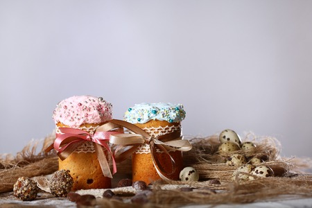 Two cakes or cupcakes with blue and pink icing on a gray or white background. The end of the Easter...