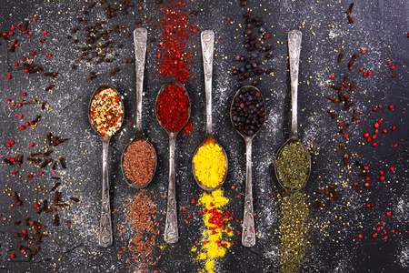Six table vintage spoons, filled with various seasonings and spices on a dark background. Seasonings and spices are scattered on a dark background.の写真素材