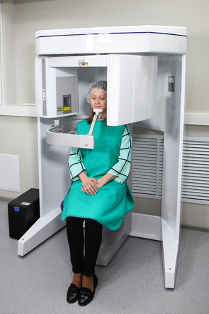 A patient at a dental clinic takes a panoramic picture of the jaw. Modern technologies in dentistry and medicine. The concept of health and beauty.The hands of the doctor in gloves fasten a protective vest for the x-ray procedure for the patient. The concept of beauty and health.の写真素材