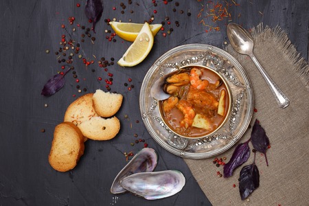 French seafood soup. Bouillabaisse ear of seafood. Vintage silver plated plate and spoon. Black background, top view. Free space for inscriptions.の写真素材