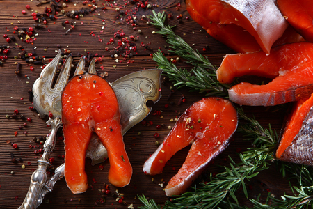 Chunks of red fish with rosemary on a wooden background with silver-plated vintage instruments. Brown background.の写真素材