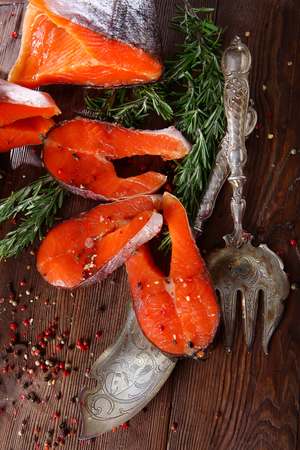 Chunks of red fish with rosemary on a wooden background with silver-plated vintage instruments. Brown background.の写真素材