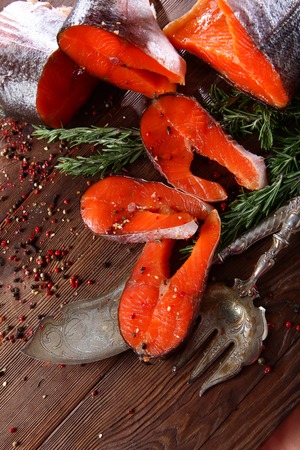 Chunks of red fish with rosemary on a wooden background with silver-plated vintage instruments. Brown background.の写真素材
