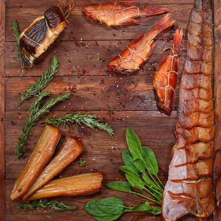 Whole smoked fish and pieces on a brown wooden background. Rosemary and spinach close up on wooden background. View from above.の写真素材
