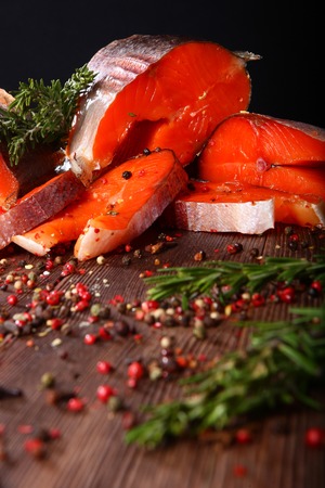 Pieces of red fish with rosemary on a wooden board on a black background. Still life concept. Still life of pieces of red fish on a black background.の写真素材