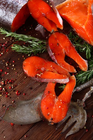 Chunks of red fish with rosemary on a wooden background with silver-plated vintage instruments. Brown background.の写真素材