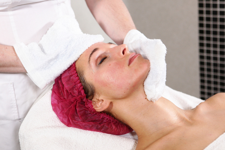 The beautician removes the anti-aging product from the patient's face. The procedure in the cosmetology clinic. The concept of beauty and health.の写真素材