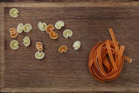Pasta nest and in assortment of yellow and orange color on a wooden background. View from above.の写真素材