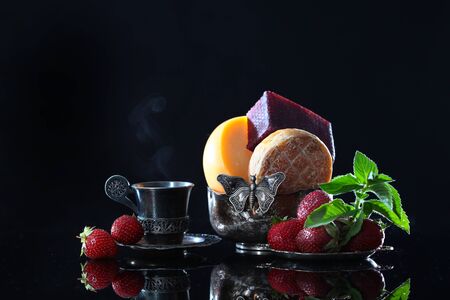 Cheese, strawberries and a vintage cup with coffee on a black background. Copy space. The concept of craft cheeses. Macro photo.の写真素材
