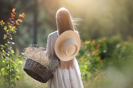 A young girl walks in the woods with a wicker basket. Photo from the back without a face. Healthy relaxation concept. Copy space.の写真素材