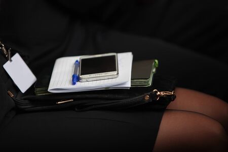 On her female lap lies a mobile phone, pen and notebook. The concept of press conferences and business meetings. Photo without a face in the interior. Badge without an inscription.の写真素材