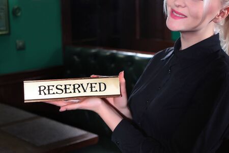 A waitress girl holds a sign that says reserve. Photo from above in the interior. Without a face.