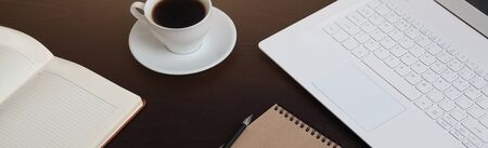 A long banner with an open notebook, a laptop and a Cup of coffee. Brown background. The concept of business in the first half of the day. The view from the top.の写真素材
