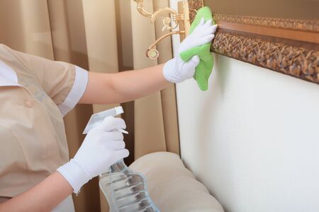 A maid dusts an unrecognizable painting. Photo without face, only hands.Copy space.