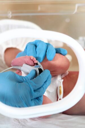 Newborn baby in intensive care. Life saving concept. Doctor hands and baby feet close-up. Photo in a medical couvez.の写真素材
