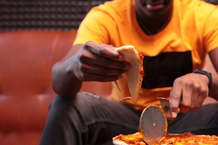 A young African-American man was cutting up a pizza. Knife for pizza in hand. Unrecognizable photo...