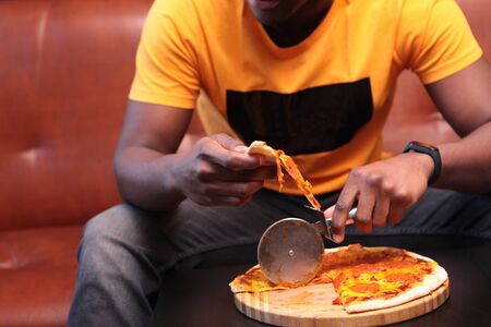 Close-up of the hands of a black young man holding a pizza and a pizza knife. The view from the top. Copy space.の写真素材