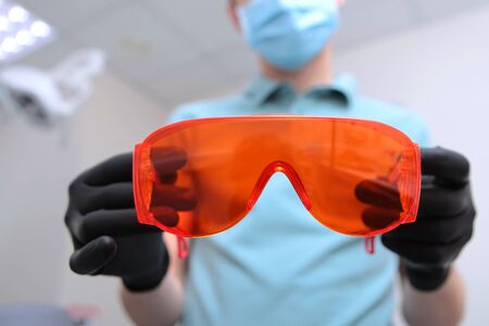 Orange safety glasses in the hands of a dentist. Unrecognizable photo. Copy space.