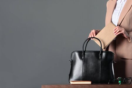 A woman's hand puts a business notebook in her bag. An unrecognizable photo. A horizontal photo with a neutral gray background. Copy space.の写真素材