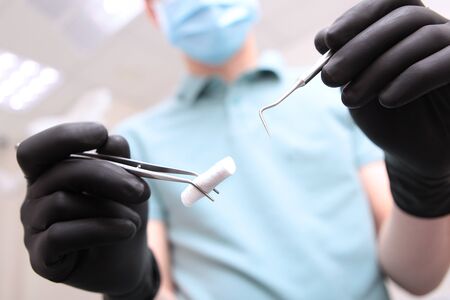 Dentist's hands in black latex gloves with medical instruments . Face out of focus. POV. Copy space.の写真素材