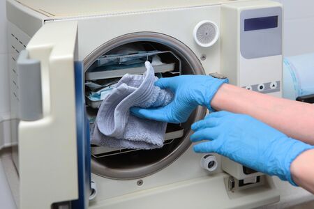 An employee of a dental clinic sterilizes instruments in a heat-resistant Cabinet. The concept of sterility and hygiene in clinics. An unrecognizable photo without a face. Copy space.の写真素材