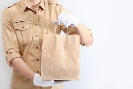 A man in a uniform and white gloves is holding a paper shopping bag. The concept of service delivery. Advertising space. Copy space.の写真素材